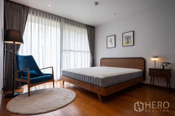 คอนโด ให้เช่าหรือขายในPathum Wan, Bangkok - ห้องนอนใหญ่พร้อมผ้าม่านเต็มผนัง เตียงไม้ และเก้าอี้เอนนั่ง