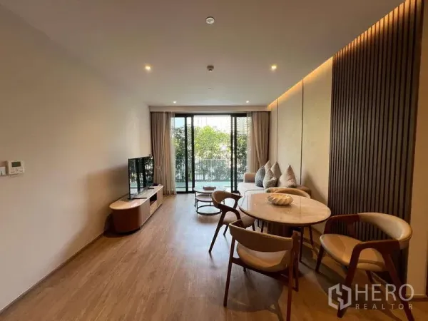 คอนโด ให้เช่าในWatthana, Bangkok - ห้องนั่งเล่นและรับประทานอาหารแบบโอเพ่นสเปซ ปูพื้นไม้ มีโต๊ะกลม โซฟา และประตูกระจกเปิดสู่ระเบียงวิวต้นไม้