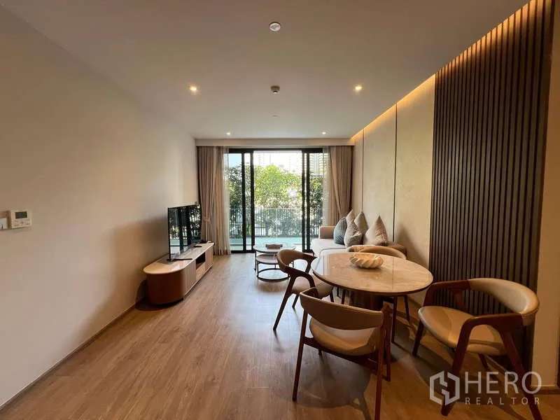 คอนโด ให้เช่าในWatthana, Bangkok - ห้องนั่งเล่นและรับประทานอาหารแบบโอเพ่นสเปซ ปูพื้นไม้ มีโต๊ะกลม โซฟา และประตูกระจกเปิดสู่ระเบียงวิวต้นไม้