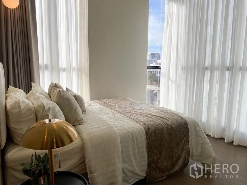 Condominium for rent in Ratchathewi, Bangkok - Bedroom with elegant bedding, bedside lamp and tall glazing offering city views.