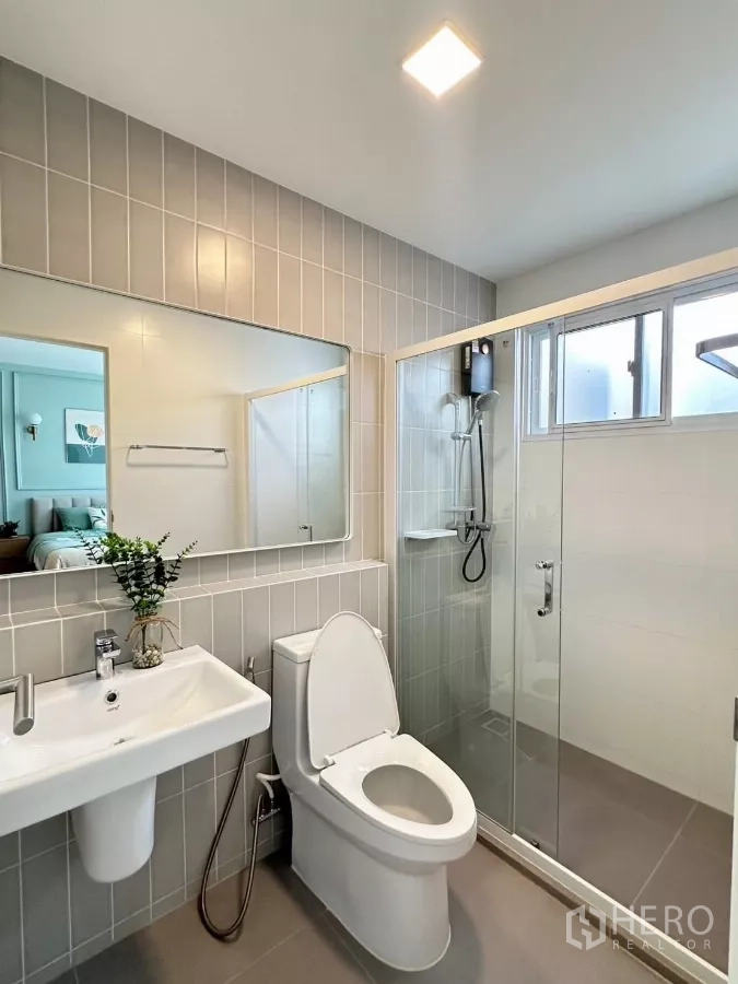 联排别墅 出租在Prawet, Bangkok - 浴室，大镜面、玻璃淋浴间与灰色瓷砖。