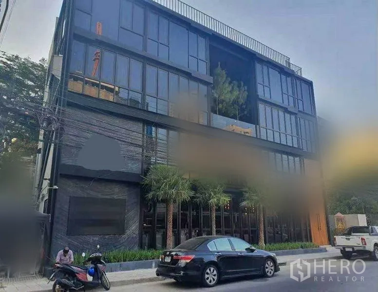 พื้นที่ขายปลีก ให้เช่าในWatthana, Bangkok - มุมมองด้านหน้าช่วงกลางวันของอาคารพาณิชย์โลว์ไรส์ พร้อมต้นปาล์มและที่จอดรถริมทาง