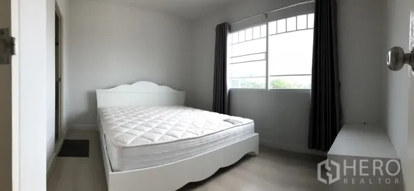 Townhouse for rent in Bang Bo, Samut Prakan - Sunlit bedroom with large window, white bed frame and curtains.