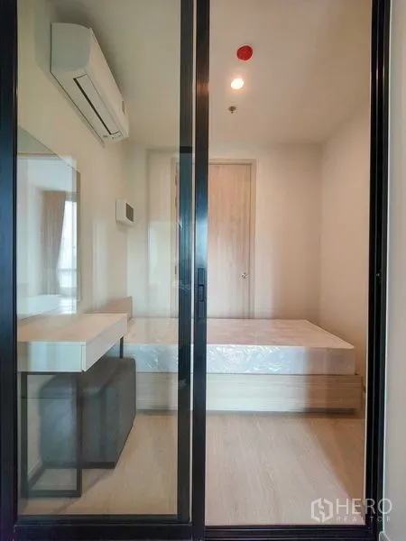 Condominium for rent - Compact bedroom behind sliding glass doors with bed base, vanity and wall-mounted air conditioner.