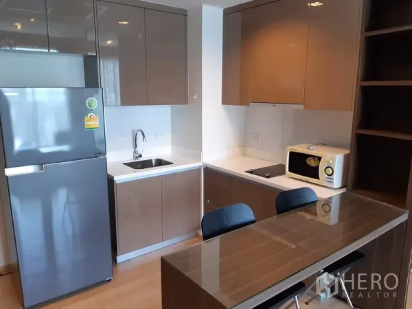 Condominium for rent in Khlong Toei, Bangkok - Modern condo kitchen with glossy cabinets, sink, cooktop, fridge and a breakfast bar.