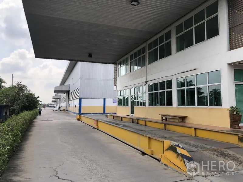 Warehouse for rent in Phra Nakhon Si Ayutthaya - Covered loading dock beside a glass-front office wing and landscaped verge.