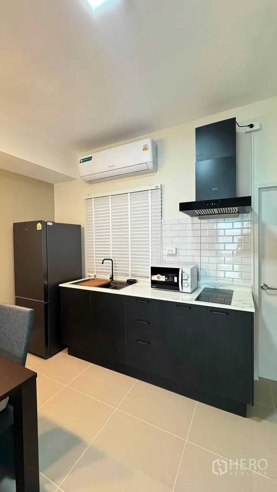 Townhouse for rent in Bang Phli, Samut Prakan - Fitted kitchen with black cabinets, marble countertop, fridge, microwave, cooktop and hood.