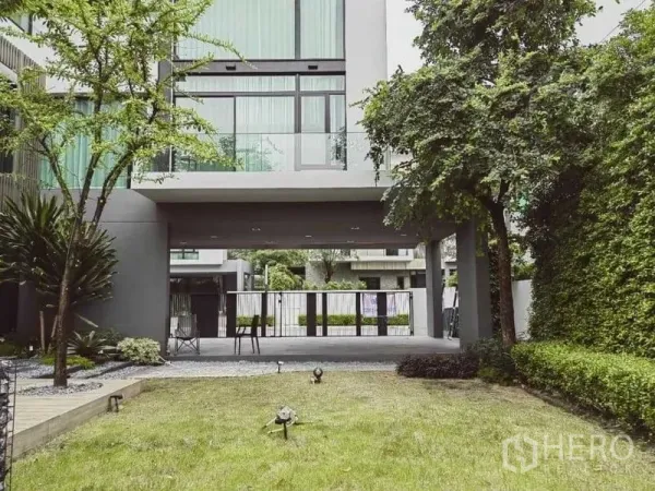 บ้าน ให้เช่า - สนามหญ้านำสู่ที่จอดรถมีหลังคา ใต้ชั้นบนยื่นลอย รายล้อมด้วยแนวรั้วต้นไม้.