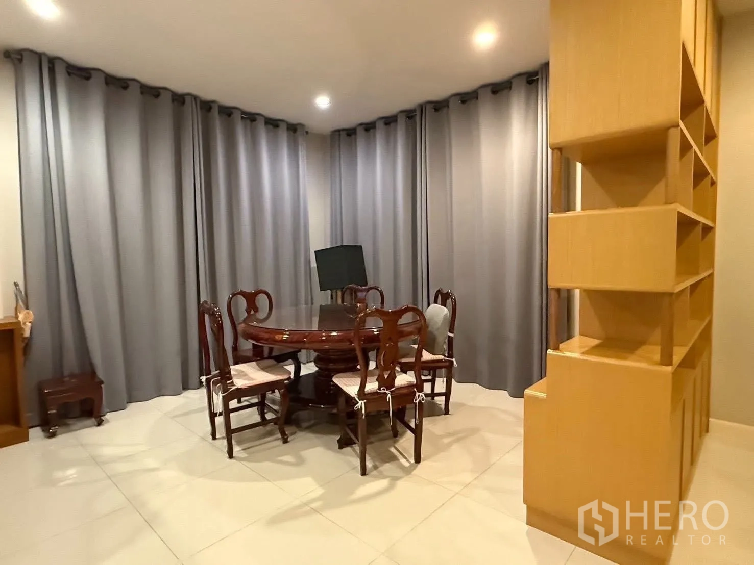 Detached House for rent in Bang Na, Bangkok - Dining room with round wooden table and chairs framed by full-height curtains.
