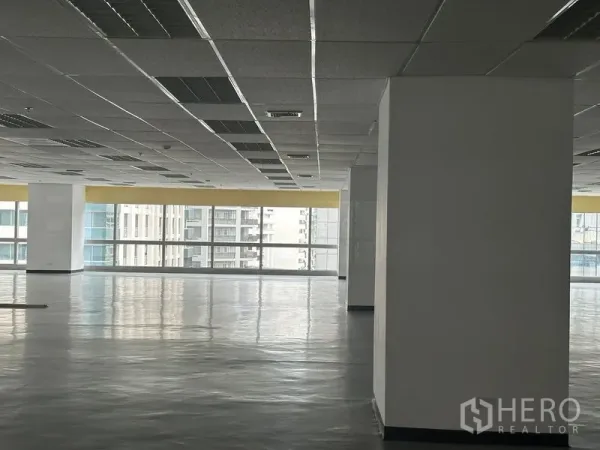 สำนักงาน ให้เช่า - มุมพื้นที่ทำงานสว่าง มีเสาค้ำและหน้าต่างกระจกเต็มบาน มองเห็นอาคารใกล้เคียง.