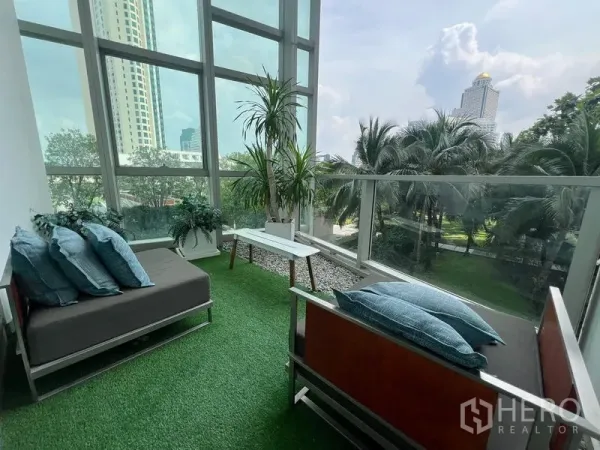 คอนโด ขายในKhlong San, Bangkok - ระเบียงปิดปูหญ้าเทียม มีเก้าอี้นั่งเล่นและวิวเมืองท่ามกลางต้นไม้