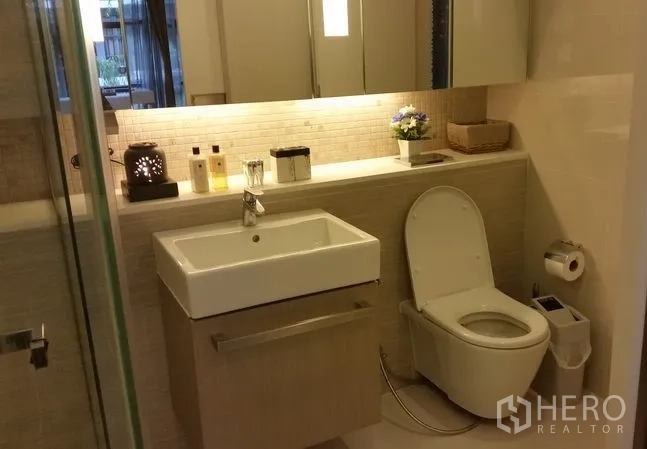 Condominium for rent or sale in Watthana, Bangkok - Contemporary bathroom with wall‑hung vanity, square sink, toilet, backlit mirror and a glass shower enclosure.