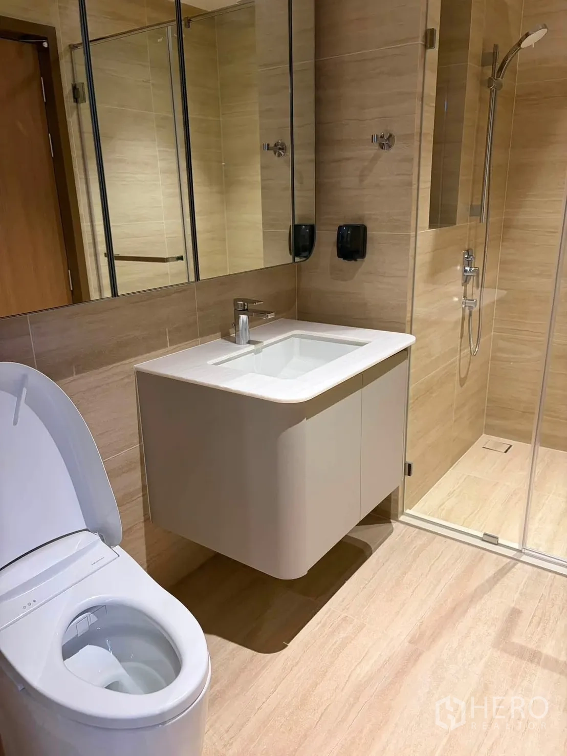 Condominium for rent in Watthana, Bangkok - Modern bathroom with wall-mounted vanity, mirrored cabinets, glass shower, and toilet.