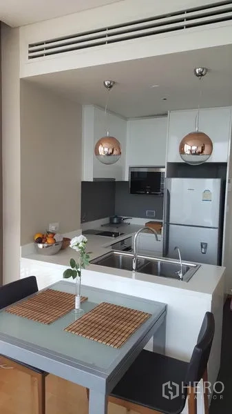 คอนโด ให้เช่าในWatthana, Bangkok - ครัวสีขาวพร้อมอ่างล้างจานคู่ โต๊ะทานข้าว และโคมไฟแขวนสีทองแดง
