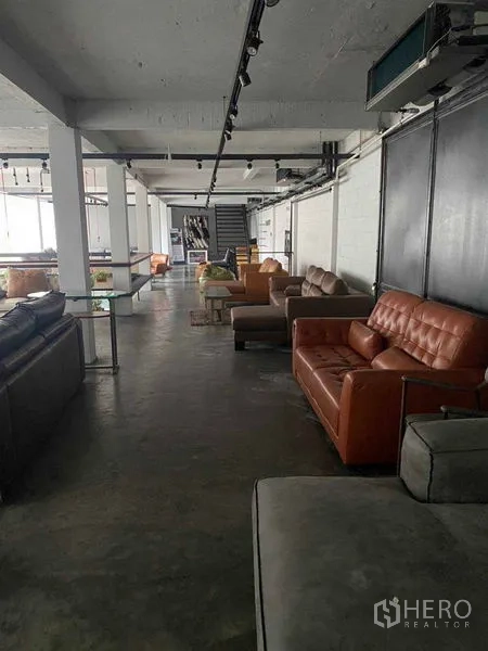 零售空间 出租在Bang Na, Bangkok - 长廊式展厅，皮沙发、轨道灯与水泥地面。