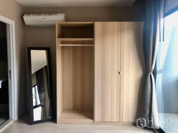 Townhouse for rent in Suan Luang, Bangkok - Bedroom corner with light wood wardrobe, wall-mounted air conditioner and a full-length mirror beside the bathroom door.