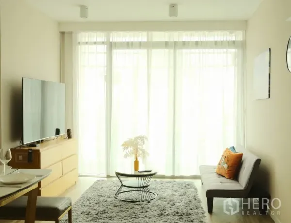 Condominium for rent in Bang Rak, Bangkok - Bright living room with floor-to-ceiling windows, gray rug, sofa, and TV unit.