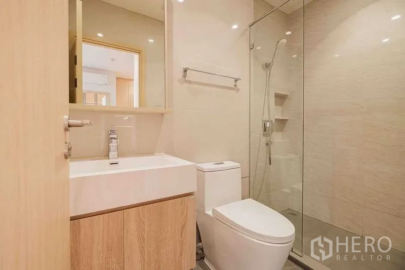 Condominium for rent in Watthana, Bangkok - Bright bathroom with wood vanity, wall mirror, and a glass-enclosed shower.