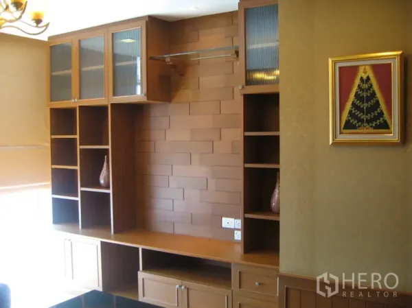 Condominium for rent in Khlong Toei, Bangkok - Built-in wooden media wall with glass-front cabinets and open shelving in a bright room.