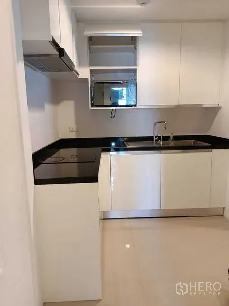 Condominium for rent or sale in Huai Khwang, Bangkok - Compact white kitchen with black granite countertops, hob, extractor and sink.