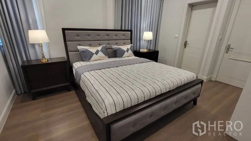 Detached House for rent or sale in Saphan Sung, Bangkok - Comfortable bedroom with striped bedding, padded headboard and two nightstands.