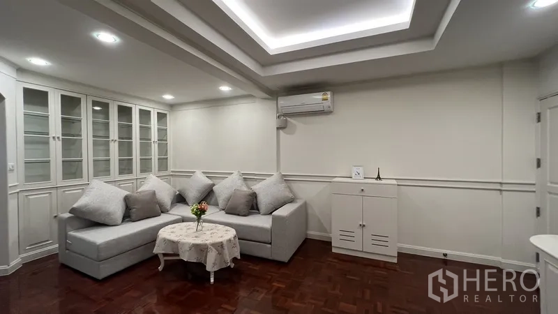 Apartment for rent in Watthana, Bangkok - Cozy lounge with built-in glass display cabinets, sectional sofa and recessed lighting.