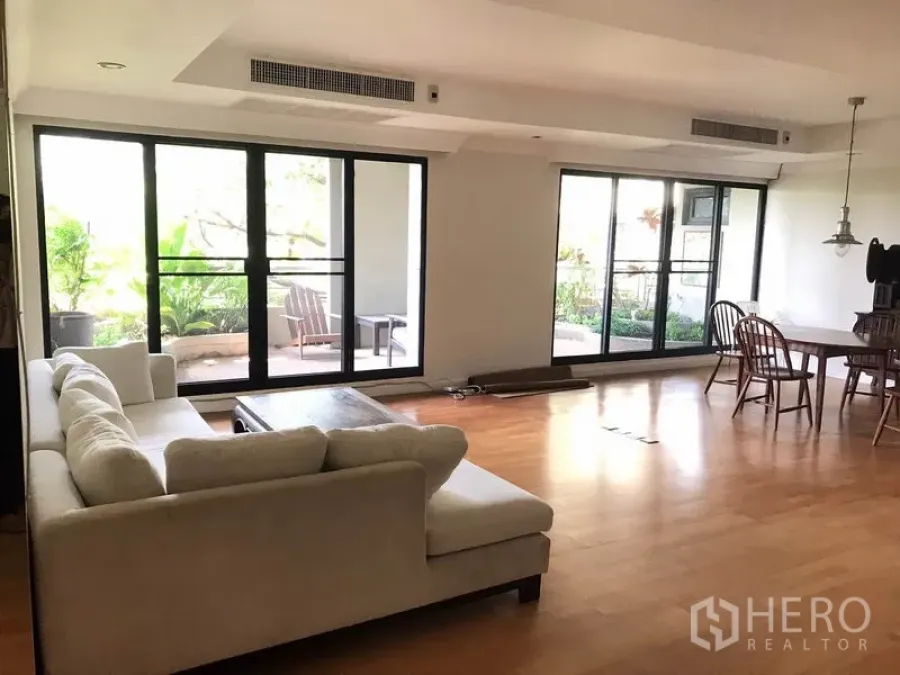 Condominium for rent in Sathon, Bangkok - Bright open-plan living room with L-shaped sofa, wood floors and sliding doors to a garden balcony in a Sathon condo.