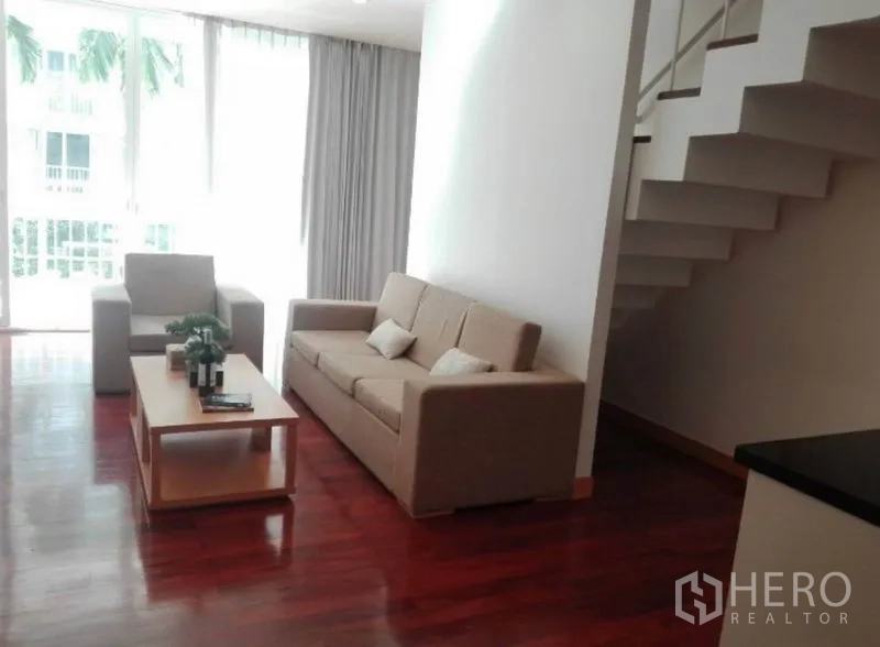 Condominium for rent in Watthana, Bangkok - Living room beside an open staircase, filled with natural light from large glazing.