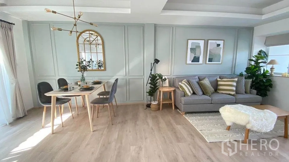 Townhouse for rent in Prawet, Bangkok - Bright open-plan living and dining room with paneled pastel walls, wood floors, gray sofa, modern chandelier and large window.