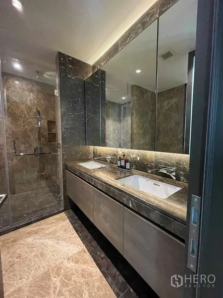 Condominium for rent in Pathum Wan, Bangkok - Luxurious bathroom with double-sink vanity, backlit mirror and glass shower.