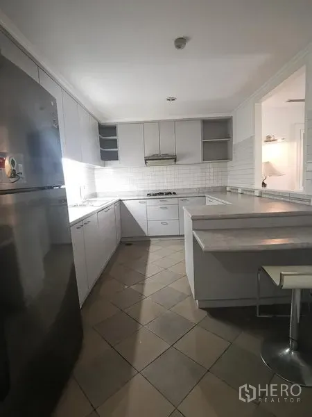 Condominium for rent in Watthana, Bangkok - U-shaped white kitchen with gas hob, tile backsplash, and breakfast counter.