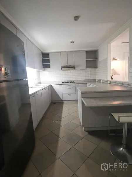 Condominium for rent in Watthana, Bangkok - U-shaped white kitchen with gas hob, tile backsplash, and breakfast counter.