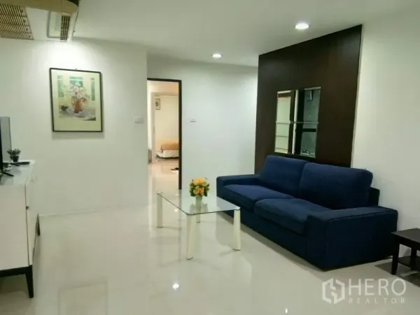 Condominium for rent in Watthana, Bangkok - Spacious lounge facing bedroom doorway with blue sofa, glass table and TV console.