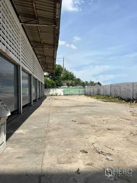 货栈 出租在Bang Na, Bangkok - 仓库侧面装卸通道，卷帘门与围墙并列，卡车可轻松进出与回转。