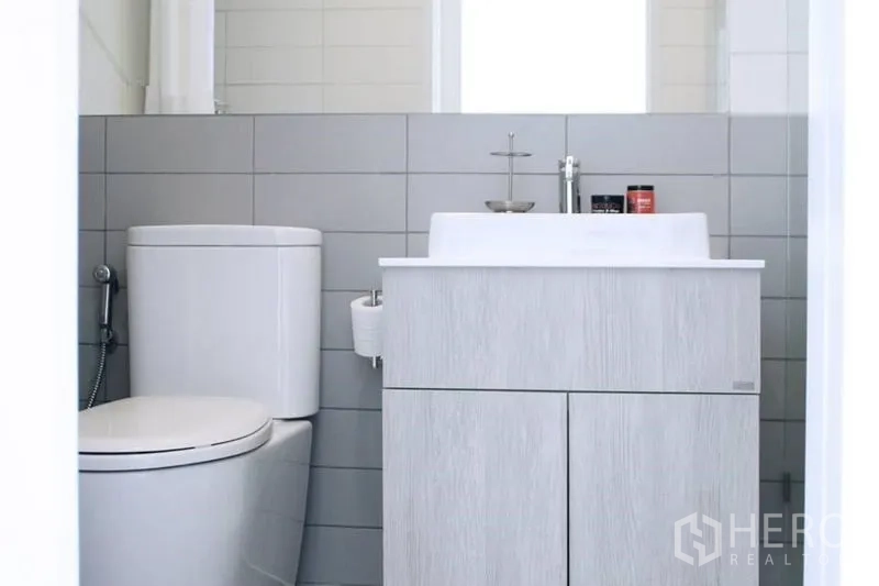 公寓 出售在Phra Khanong, Bangkok - 整洁浴室，坐便器、灰色墙砖与洗手台柜。