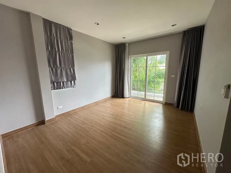 Detached House for sale in Bang Khen, Bangkok - Spacious bedroom with wood floors and large sliding glass doors with curtains.