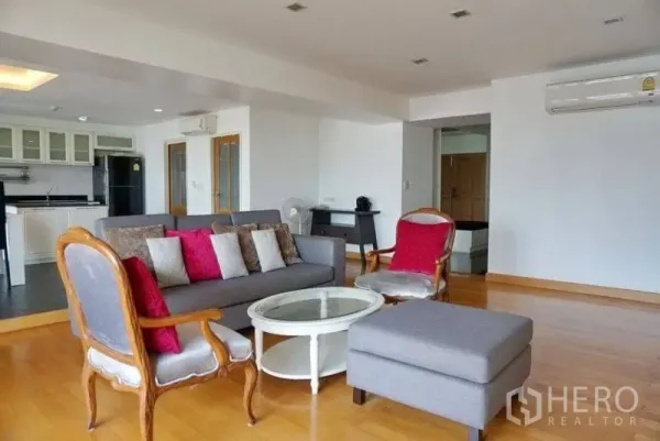 Condominium for rent in Watthana, Bangkok - Bright open-plan living room with wooden floors, gray sofa set, accent chairs and access to the kitchen.
