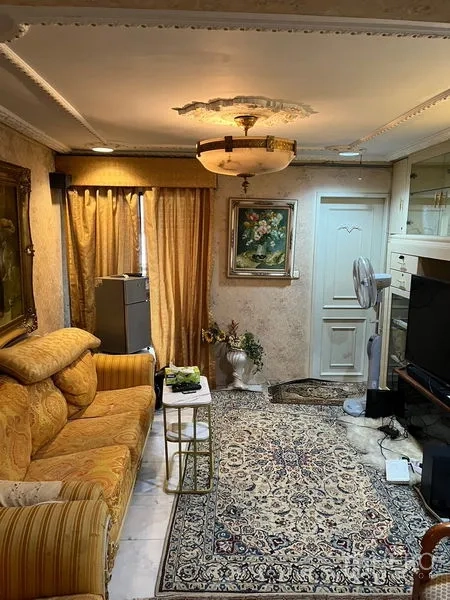 คอนโด ขายในKhlong Toei, Bangkok - มุมนั่งเล่นอบอุ่น โซฟาสีทอง พรมลาย และชั้นวางทีวี ใต้โคมไฟเพดานดีไซน์คลาสสิก