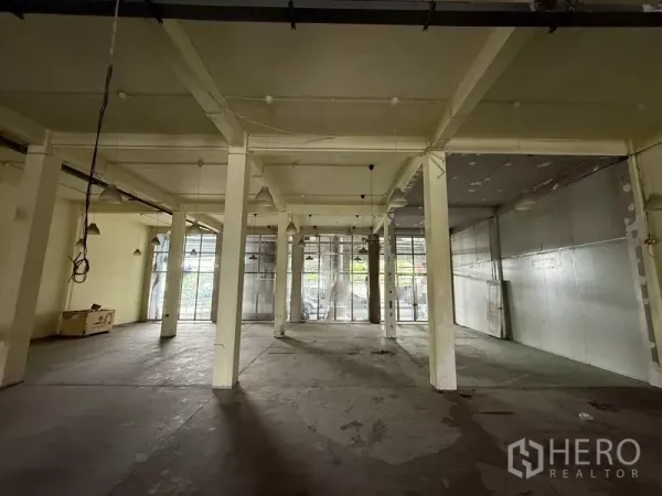 店屋 出租 - 一层开放式大厅，水泥地面、多根立柱与落地窗。