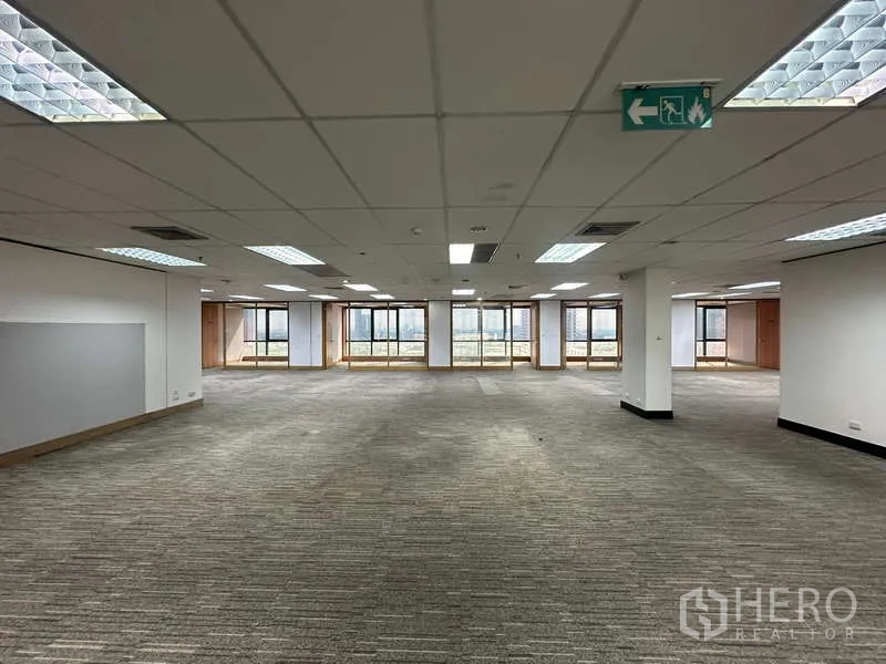 Office Space for rent in Khlong Toei, Bangkok - Large workspace with multiple windows, columns and emergency exit signage.