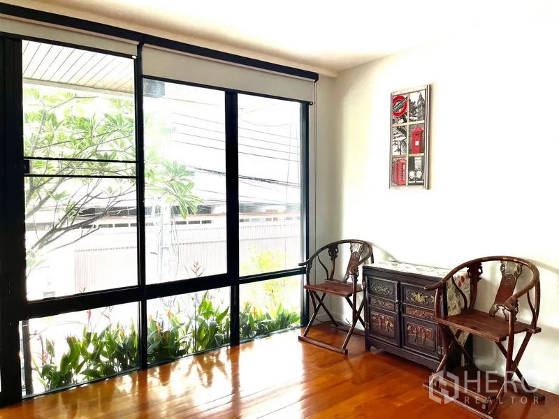 Townhouse for rent in Khlong Toei, Bangkok - Sunlit reading nook with full-height windows, two accent chairs and garden view.