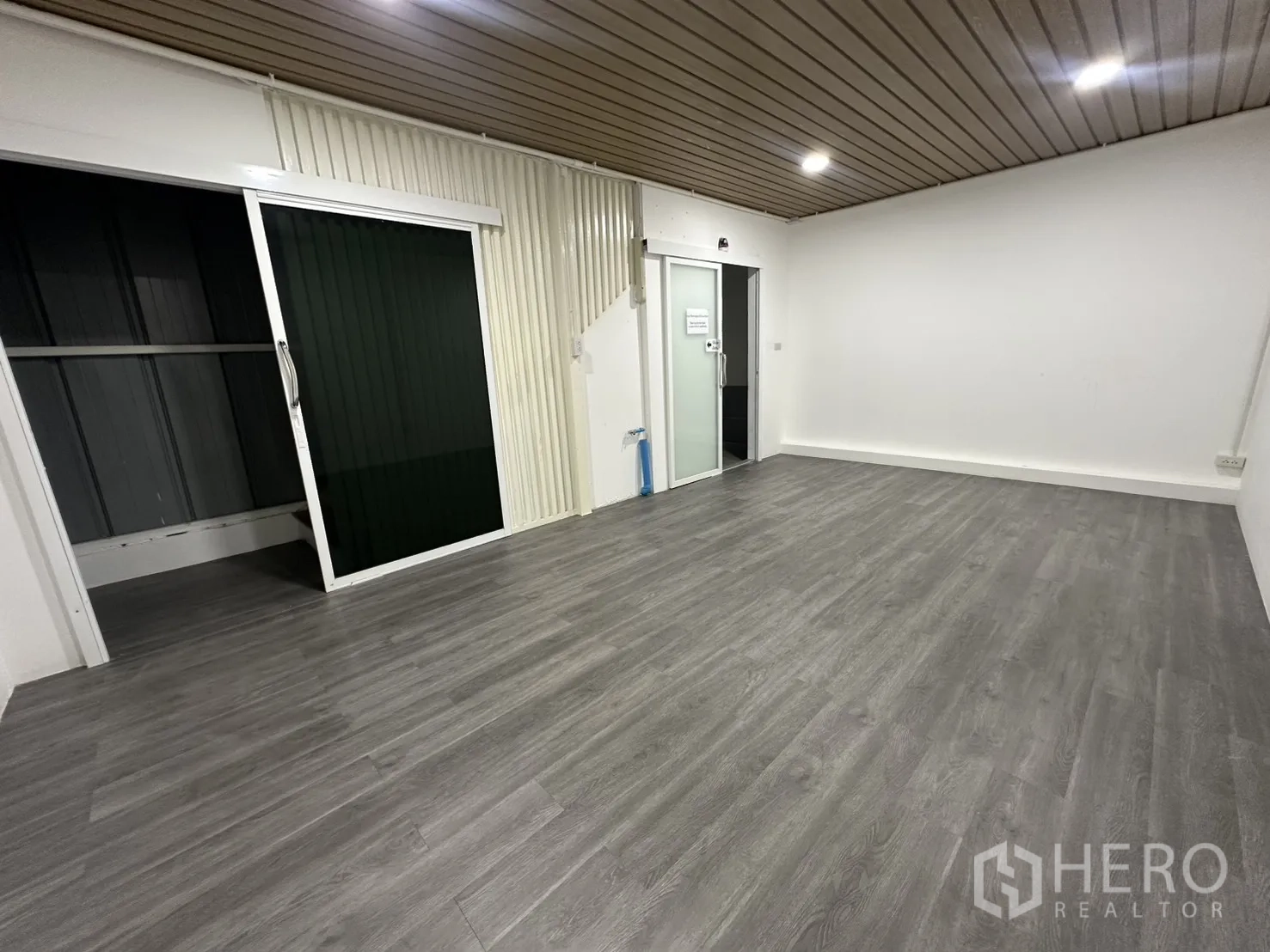 Warehouse for rent in Suan Luang, Bangkok - Ground‑floor office room with grey vinyl flooring, sliding glass doors and a slatted ceiling with downlights.