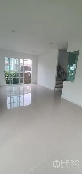 Detached House for rent in Nonthaburi - Open-plan living area with glossy floor tiles, sliding glass doors and stairway in Pak Kret, Nonthaburi.