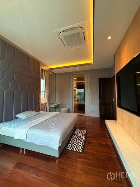Detached House for rent or sale in Bang Phli, Samut Prakan - Primary bedroom with wood floors, padded feature wall, cassette air‑conditioner and warm cove lighting.