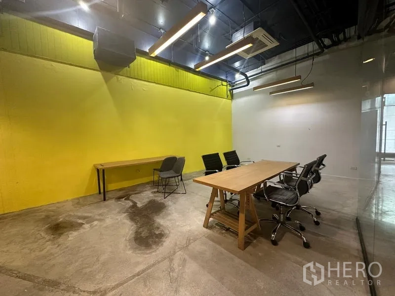 สำนักงาน ให้เช่า - โซนทำงานร่วม ผนังสีเหลือง โคมไฟแขวน และพื้นคอนกรีตขัดมัน
