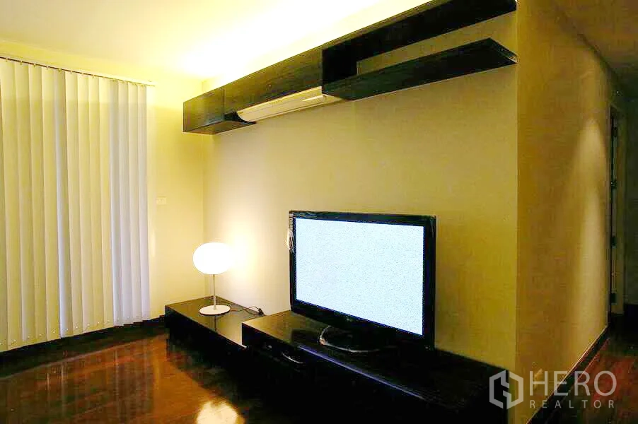 Condominium for rent in Watthana, Bangkok - Cozy TV lounge with floor lamp, vertical blinds, wall-mounted shelving and wooden floor.