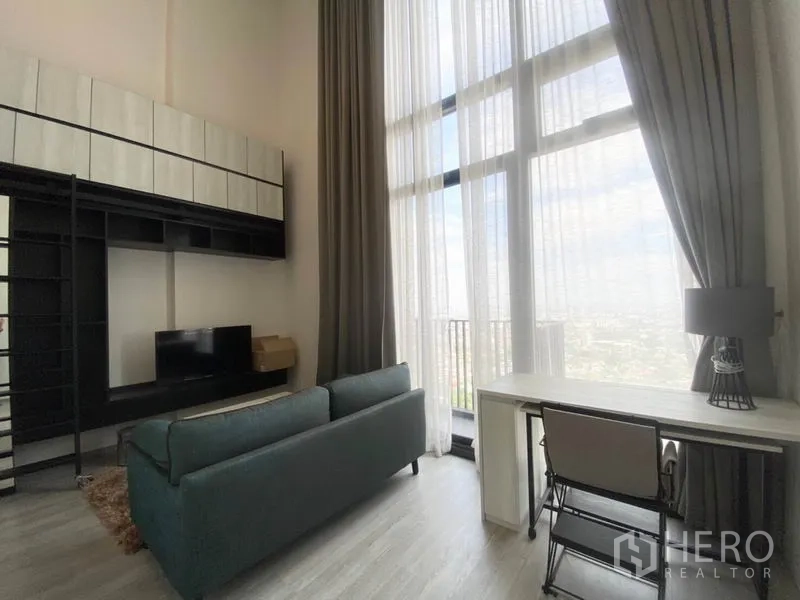 Condominium for rent in Phra Khanong, Bangkok - Bright living area with floor-to-ceiling windows, study desk and wall-mounted storage with TV.