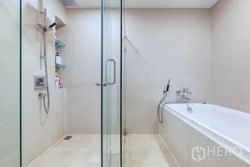 Condominium for rent in Bang Na, Bangkok - Bathroom with glass-enclosed rain shower and separate bathtub in light tiles.