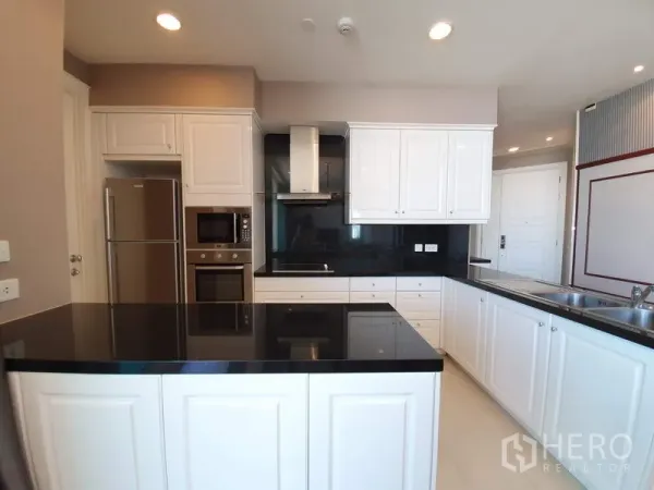 公寓 出租在Watthana, Bangkok - 现代白色厨房，黑色石材台面与中岛，嵌入式烤箱微波炉和不锈钢冰箱。