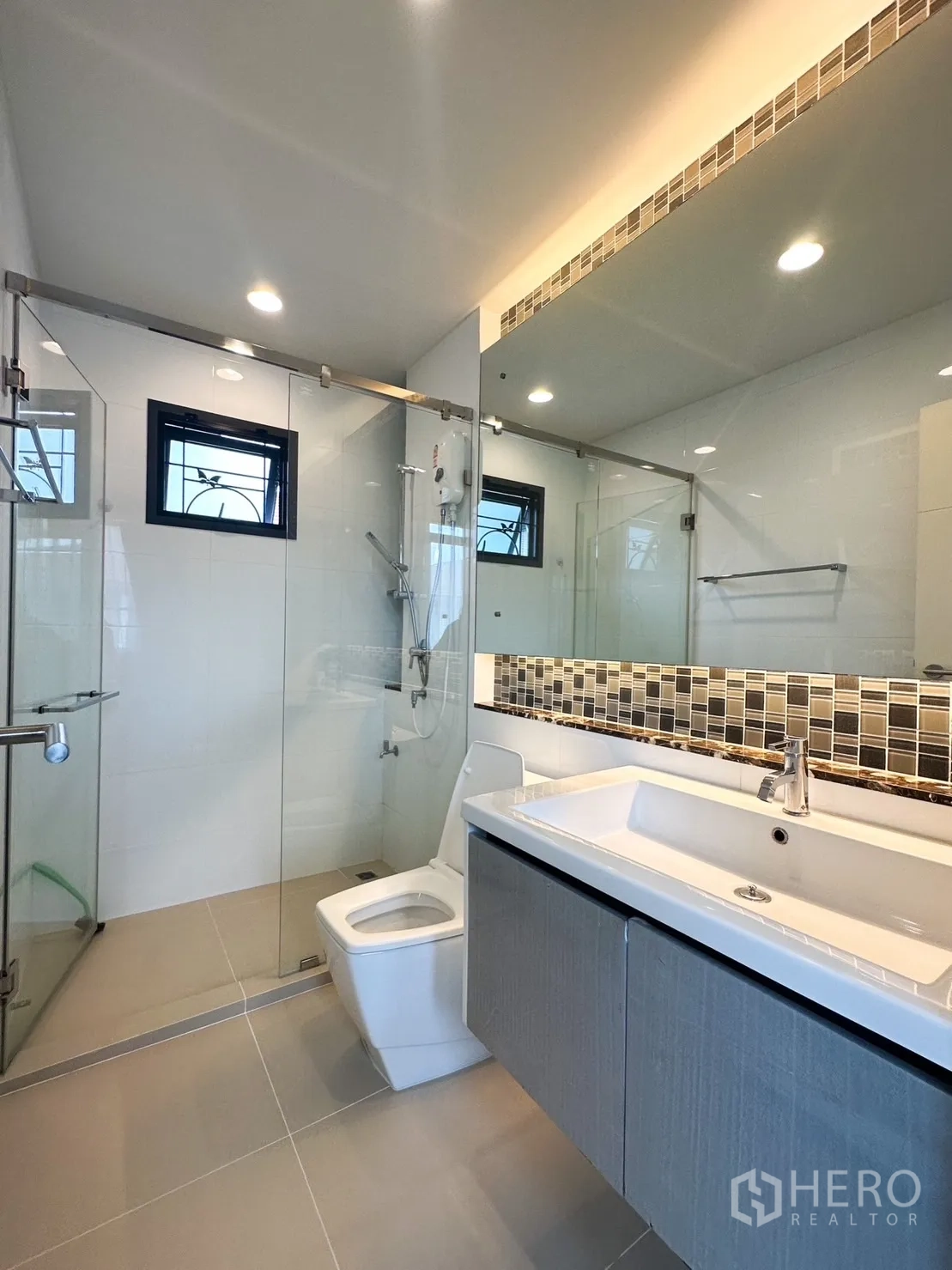 Detached House for rent or sale in Bang Kapi, Bangkok - Modern bathroom with glass shower, long mirror and wall-hung vanity.